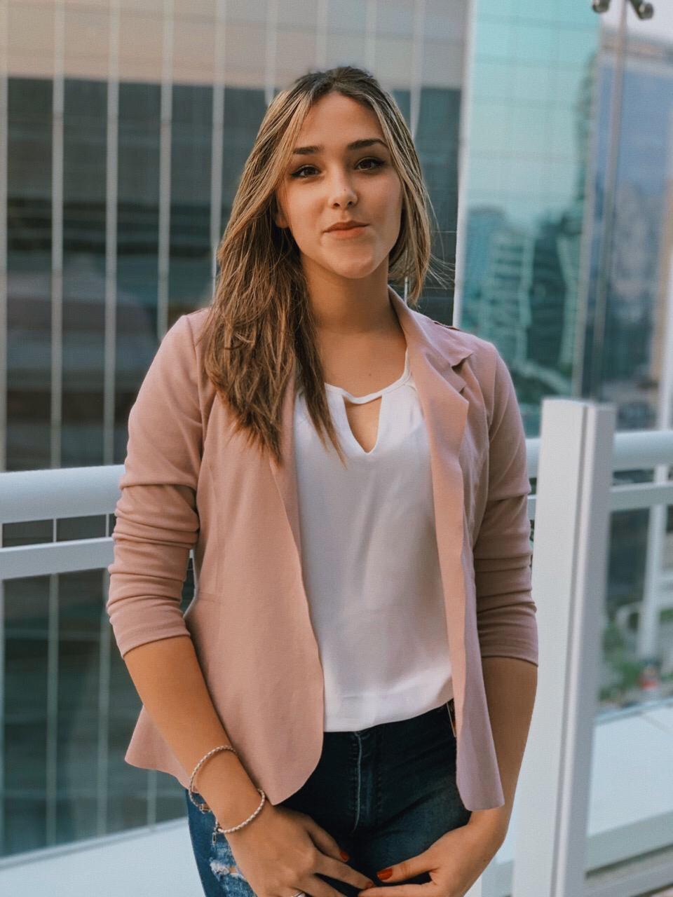 Foto de uma mulher vestindo calça jeans, camiseta branca e jaqueta rosa