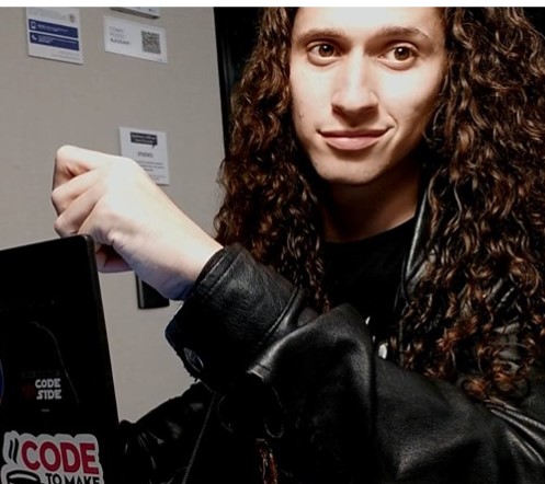 Foto de um homem, segurando um computador e vestindo jaqueta de couro preta